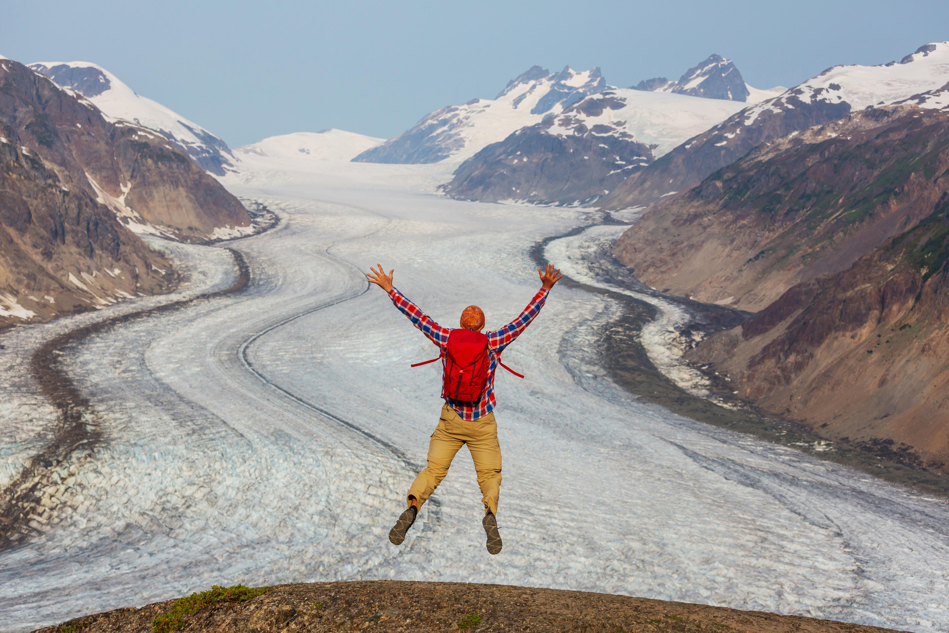 Un homme sautant devant un glacier